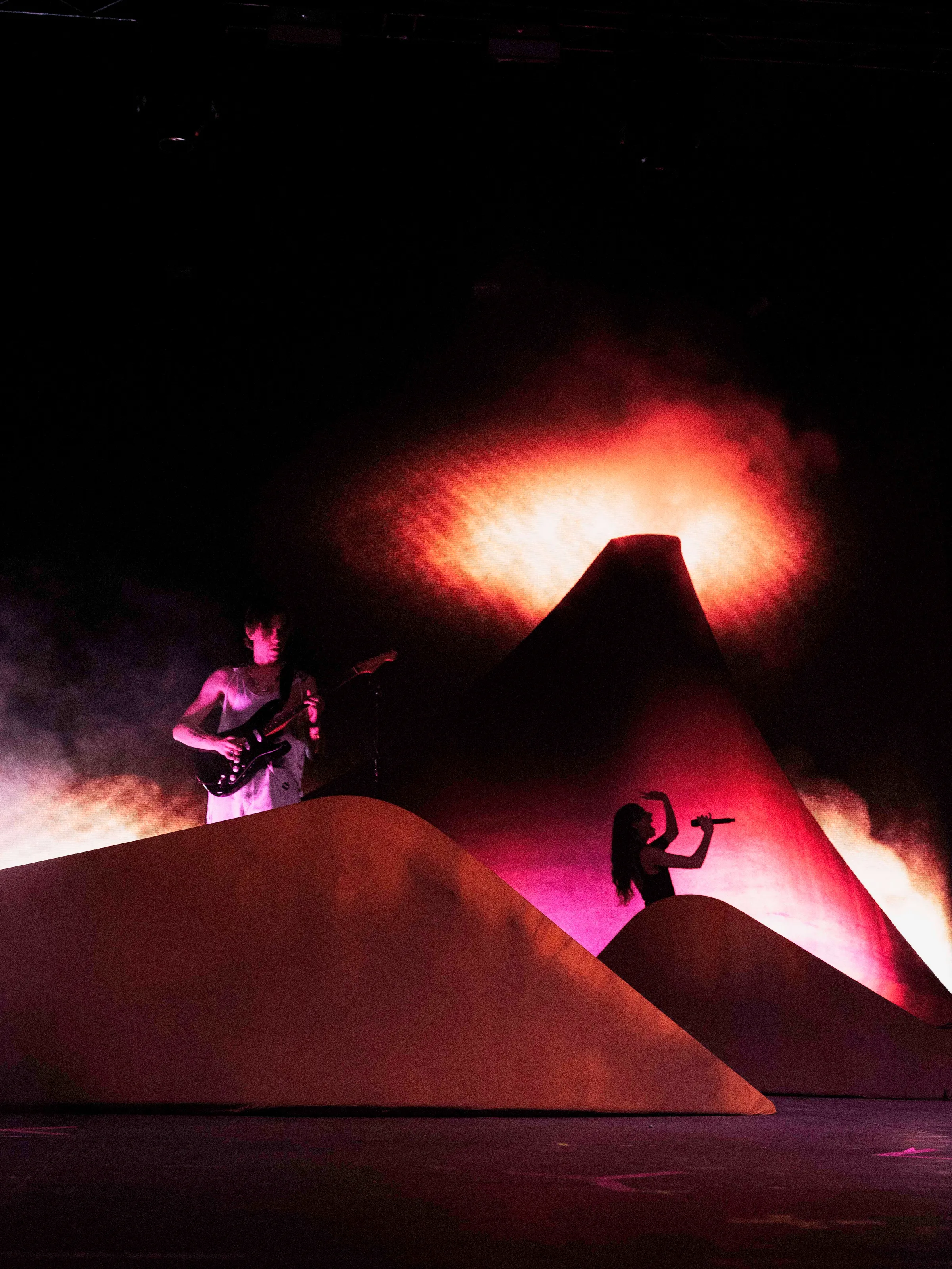 Caroline Polachek and a guitarist performing under red stage light.
