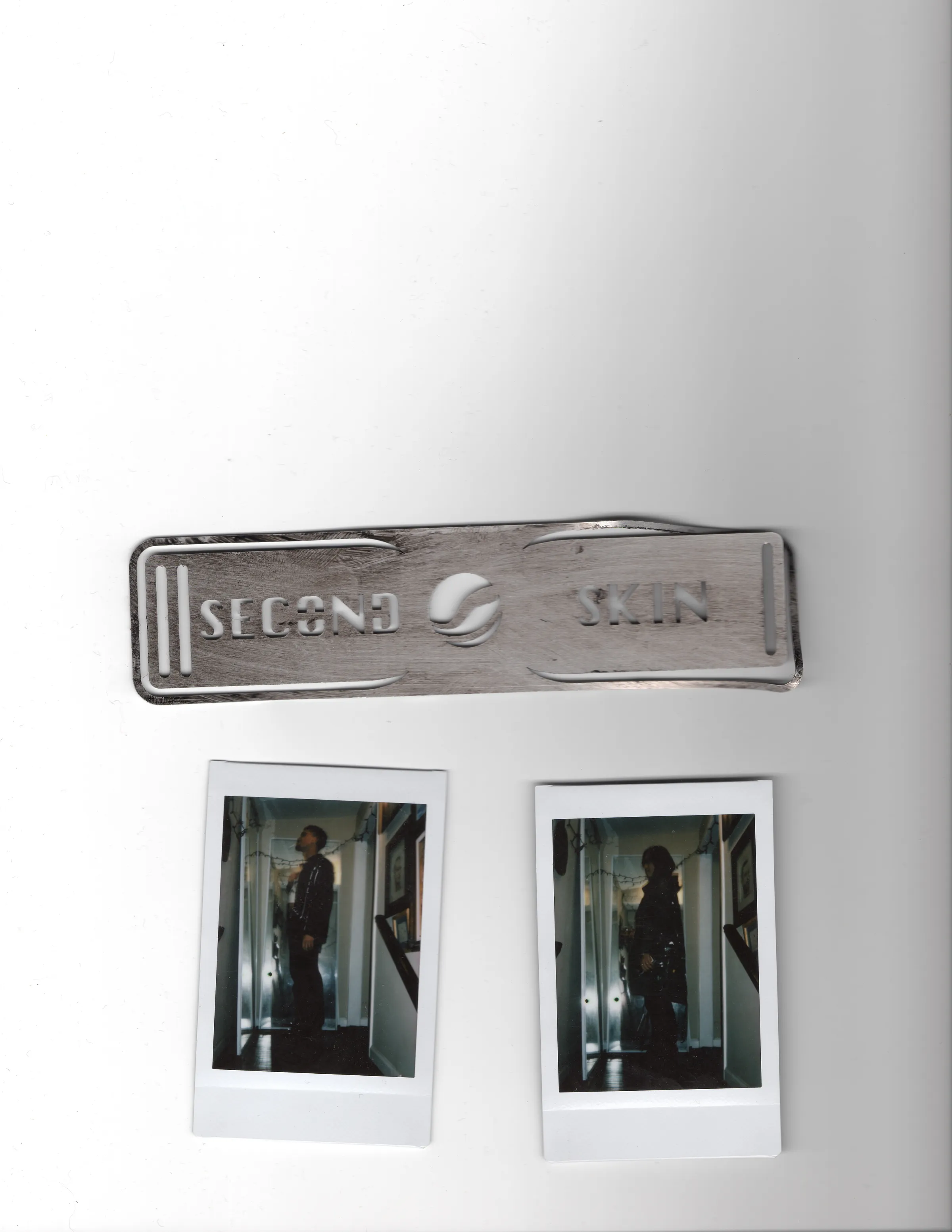 A brushed metal Second Skin tag above two Polaroids.