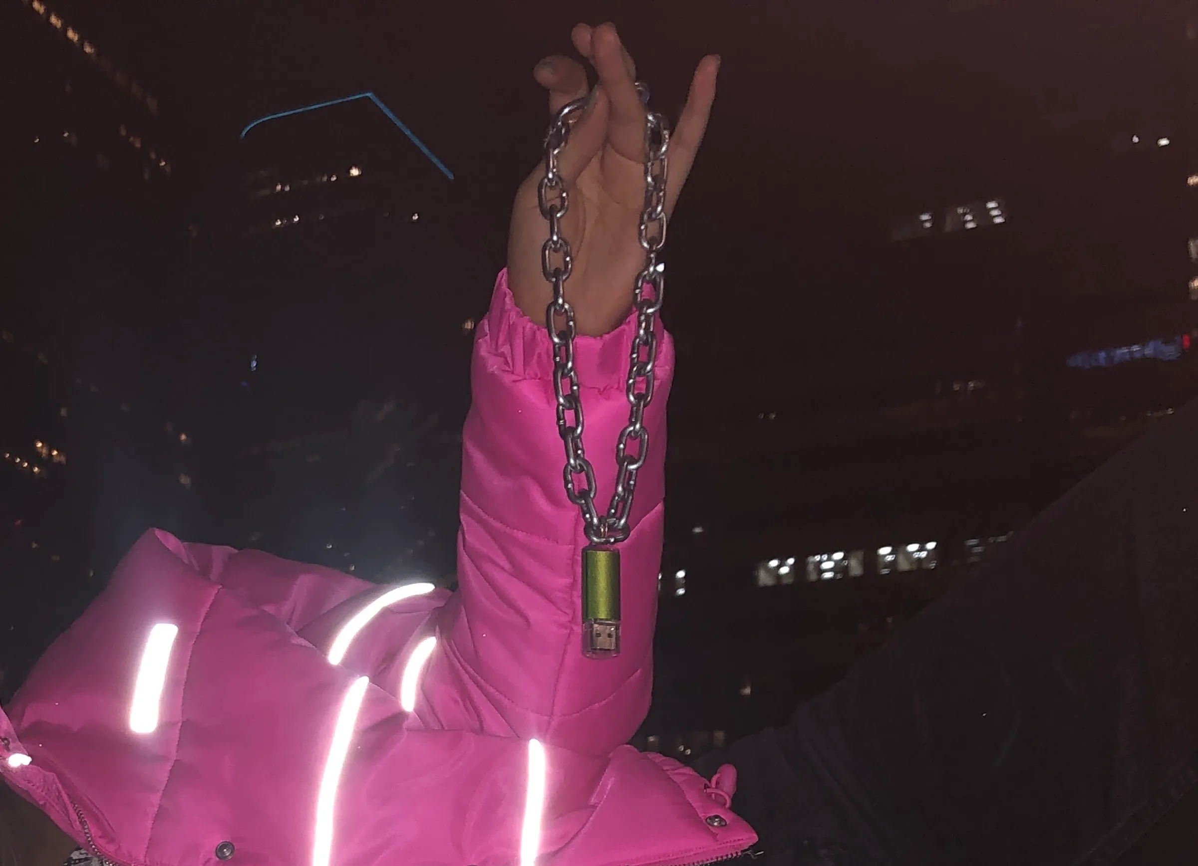 A green USB chain held aloft at night against a reflective pink jacket.